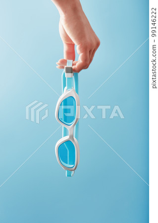 White swimming glasses in hand on a blue background 99146222