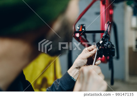 Mechanic repairman assembling brake cable custom bicycle in workshop Mechanic repairman assembling brake cable custom bicycle in workshop 99147135