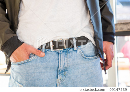 Man wearing jacket and jeans with stylish black leather belt. Close-up of craft accessory. Fashion and casual modern style Man wearing jacket and jeans with stylish black leather belt. Close-up of craft accessory. Fashion and casual modern style 99147389