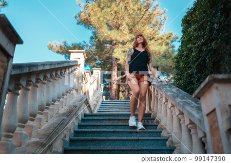 Summertime and travel. A young tanned woman with tattoos is walking down the stone steps. Bottom view Summertime and travel. A young tanned woman with tattoos is walking down the stone steps. Bottom view 99147390