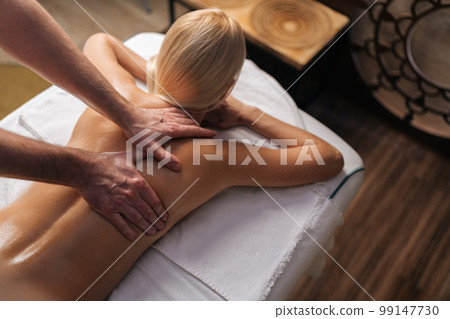 Top view of unrecognizable relaxed woman lying down on massage table with during back neck massage at spa salon. Male masseur massaging shoulders. Concept of healthy lifestyle and body care. Top view of unrecognizable relaxed woman lying down on massage table with during back neck massage at spa salon. Male masseur massaging shoulders. Concept of healthy lifestyle and body care. 99147730