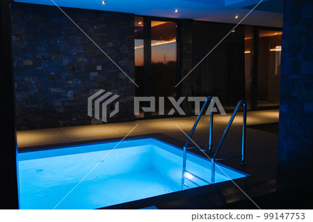 Plunge pool with cold water preparing after relaxing in sauna. Pool is filled with water. Evening photo with backlight 99147753