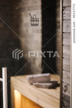 Finnish bathroom with a small wooden sauna. Modern spa interior with glass door. Photo through the glass door Finnish bathroom with a small wooden sauna. Modern spa interior with glass door. Photo through the glass door 99147772