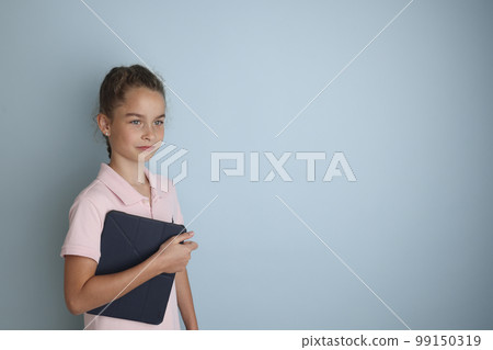 Little emotional teenage girl in pink shirt 11, 12 years old on an isolated blue background with a tablet in her hands.Children's studio portrait. Place the text to copy the place for the inscription Little emotional teenage girl in pink shirt 11, 12 years old on an isolated blue background with a tablet in her hands.Children's studio portrait. Place the text to copy the place for the inscription 99150319