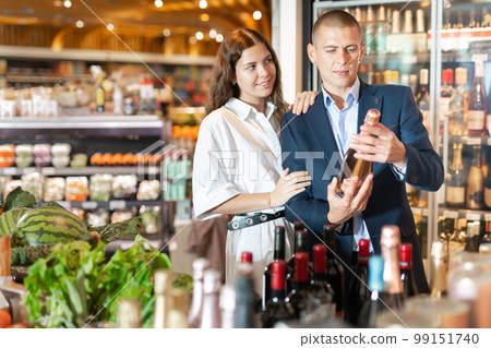 Young couple in the supermarket chooses a bottle of champagne 99151740