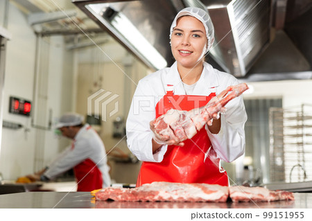 Female butchery worker offering fresh raw lamb leg 99151955