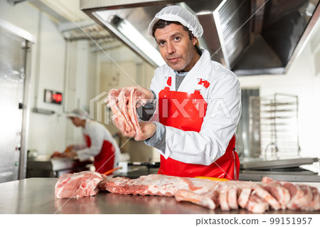 Male meat seller demonstrating raw pork ribs 99151957