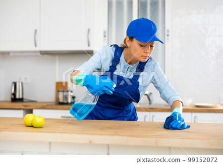 Skilled woman house cleaner sanitizing kitchen countertop 99152072