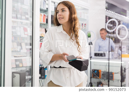 Young woman choosing phone in consumer electronics store 99152073