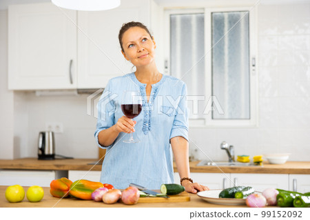 Woman with glass of wine in kitchen Woman with glass of wine in kitchen 99152092