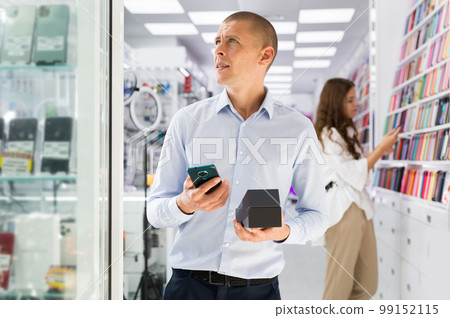 Smiling male holding mobile phone in the hand at electronics store 99152115