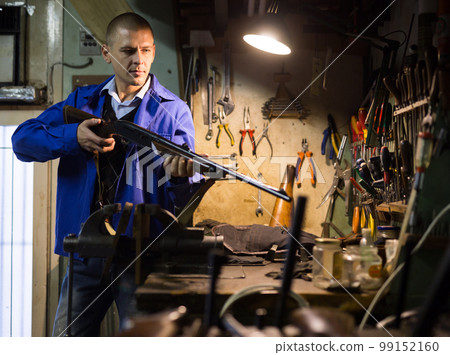 Gun repairman examining hunting shotgun before repair in workshop Gun repairman examining hunting shotgun before repair in workshop 99152160
