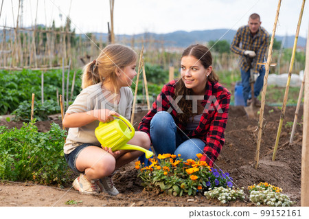 Positive child with her mother caring for flowers at a garden Positive child with her mother caring for flowers at a garden 99152161