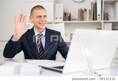 Businessman having video call on laptop and waving hand 99152216
