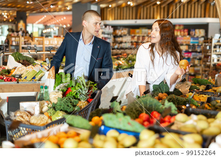 Glad couple is standing with cart with products in supermarket Glad couple is standing with cart with products in supermarket 99152264