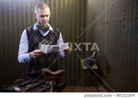 Man looking at paper target checking target hit at firing range 99152304