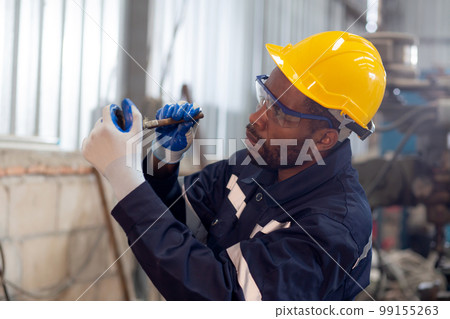 Young black engineer man examining and measuring steel with expertise at lathe factory. 99155263
