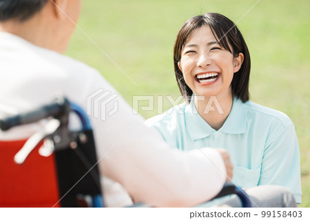 Caregiver working with a smile / Female caregiver talking to a man in a wheelchair 99158403