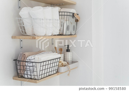 Beautiful white bathroom. Wooden shelves. Rolled towels, stacked towels and baskets. Soap, washcloth 99158580