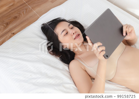 happy asian woman lie down and playing tablet relax time at bedroom. happy asian woman lie down and playing tablet relax time at bedroom. 99158725