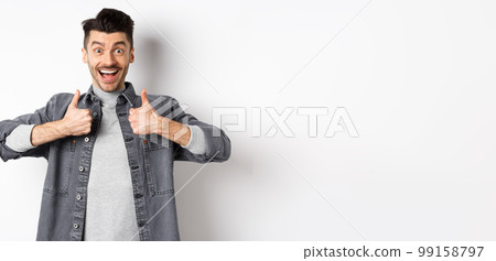 Sounds great. Excited young man showing thumbs up and smiling happy, recommending cool thing, praise nice job, standing on white background 99158797