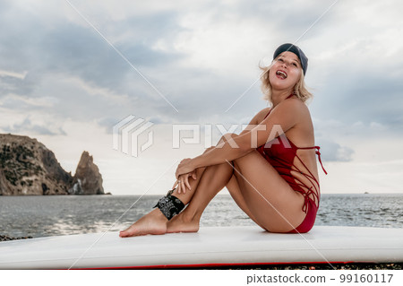 Woman in red bikini on Beach. Happy lady with blond hair in bathing suit chilling and sunbathing by turquoise sea ocean on sunset. Holiday, vacation and recreational concept. Close up Woman in red bikini on Beach. Happy lady with blond hair in bathing suit chilling and sunbathing by turquoise sea ocean on sunset. Holiday, vacation and recreational concept. Close up 99160117
