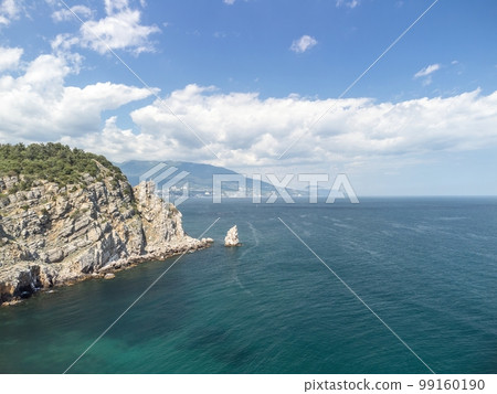 aerial photo of rock Parus Sail and Ayu-Dag Bear Mountain and near Gaspra, Yalta, Crimea at bright sunny day over the Black sea. Rock Parus in Gaspra near Swallow's nest in Crimea. 99160190