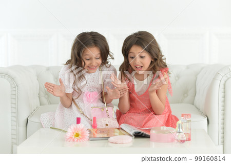 Cute sisters sitting on sofa with magazine and cosmetics 99160814