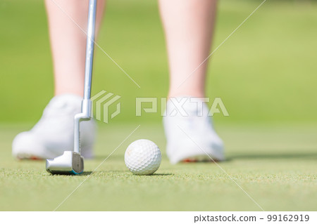 Female golfer about to hole in a cup on a golf course using a putter 99162919
