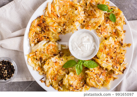 Vegetable fritters from cabbage and carrots and sauce on a plate. Vegetarian food. Top view. Closeup Vegetable fritters from cabbage and carrots and sauce on a plate. Vegetarian food. Top view. Closeup 99165097