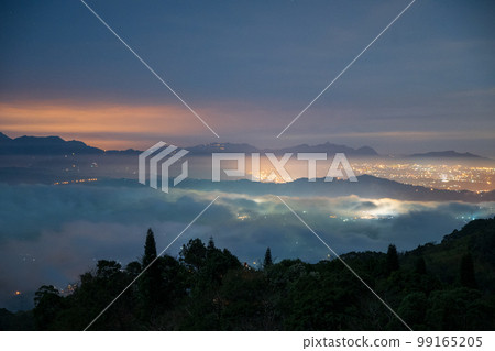 Night view of city lights in the valley. Spectacular cloud waterfall in the sky. 99165205