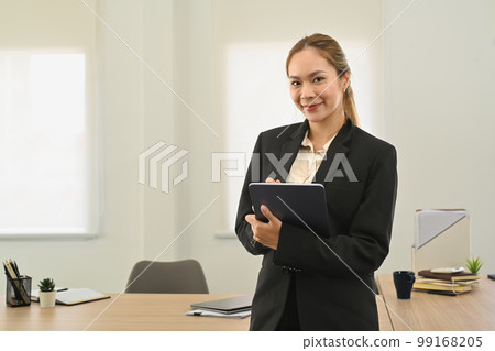 Gorgeous businesswoman with digital tablet in hands standing in corporate office and smiling to camera 99168205
