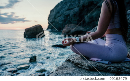 Young woman with black hair, fitness instructor in pink leggings and tops doing stretching and pilates on volcanic rocks near the sea on sunset. Female fitness yoga routine concept. Healthy lifestyle. 99168479