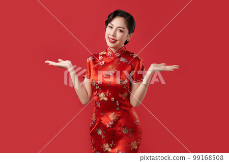 Happy Chinese new year, Beautiful young Asian woman wearing traditional cheongsam qipao dress with gesture of introduce isolated on red background, 99168508