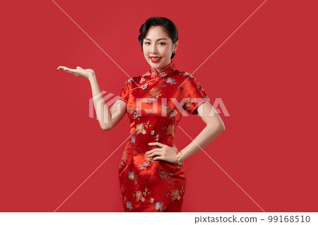 Happy Chinese new year, Beautiful young Asian woman wearing traditional cheongsam qipao dress with gesture of introduce isolated on red background, 99168510