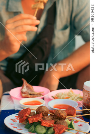 A tourist eating one of the skewers from a plate full of different khmer street food skewers or mhoup taam phlew A tourist eating one of the skewers from a plate full of different khmer street food skewers or mhoup taam phlew 99169438