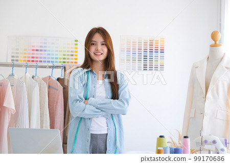 A young asian female fashion designer is standing with arms folded confident and looking at camera in her design studio. A young asian female fashion designer is standing with arms folded confident and looking at camera in her design studio. 99170686