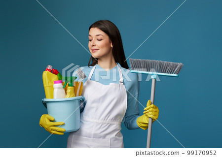 woman in cleaner apron holding bucket of detergents and broom 99170952