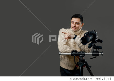 photographer in sweater near digital camera on tripod 99171071