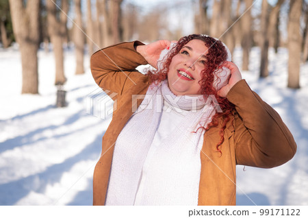 Cheerful fat caucasian woman in fur headphones outdoors. Cheerful fat caucasian woman in fur headphones outdoors. 99171122