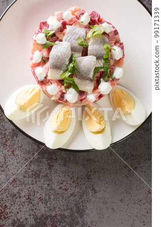 Sillsallad Herring salad with vegetables dressed with sour cream and decorated with boiled eggs close-up in a plate. vertical top view Sillsallad Herring salad with vegetables dressed with sour cream and decorated with boiled eggs close-up in a plate. vertical top view 99171339