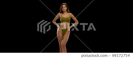 Young sensual woman with slender legs posing in olive color lingerie isolated over black background. Concept of beauty, body and skin care, health, ad 99172754