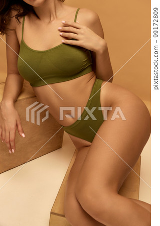 Cropped image of slim female body in green underwear isolated over beige color background. Well-being. Concept of beauty, body and skin care, health, spa, cosmetics, ad 99172809