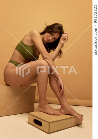 Portrait of young slim beautiful girl wearing green color underwear posing over brown background. Concept of beauty, body and skin care, healthy eating Portrait of young slim beautiful girl wearing green color underwear posing over brown background. Concept of beauty, body and skin care, healthy eating 99172823