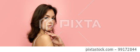 Closeup portrait of young beautiful girl with long dark hair looking at camera over pink background. Concept of beauty, skin care, cosmetology, wellness, makeup 99172844