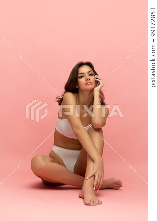Young tall thin girl with long soft brown hair wearing white inner wear posing over pink color background. Concept of natural beauty, body and skin care, healthy eating Young tall thin girl with long soft brown hair wearing white inner wear posing over pink color background. Concept of natural beauty, body and skin care, healthy eating 99172851