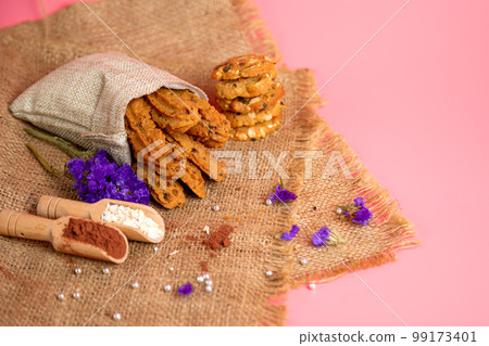 Brown cookie stick shape in burlap bag and other with flour cocoa dried flower on pink background 99173401