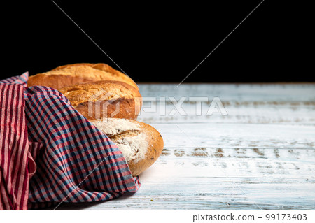 Assortment of fresh baked bread and wrapped cloth on white wooden on black background 99173403