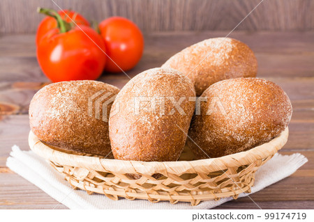 Fresh rye buns in a basket and tomato on a wooden table 99174719