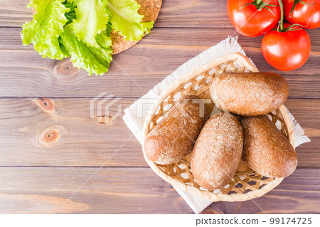 Fresh rye buns in a basket, salad and tomato on a wooden table. Top view. Copy space Fresh rye buns in a basket, salad and tomato on a wooden table. Top view. Copy space 99174725
